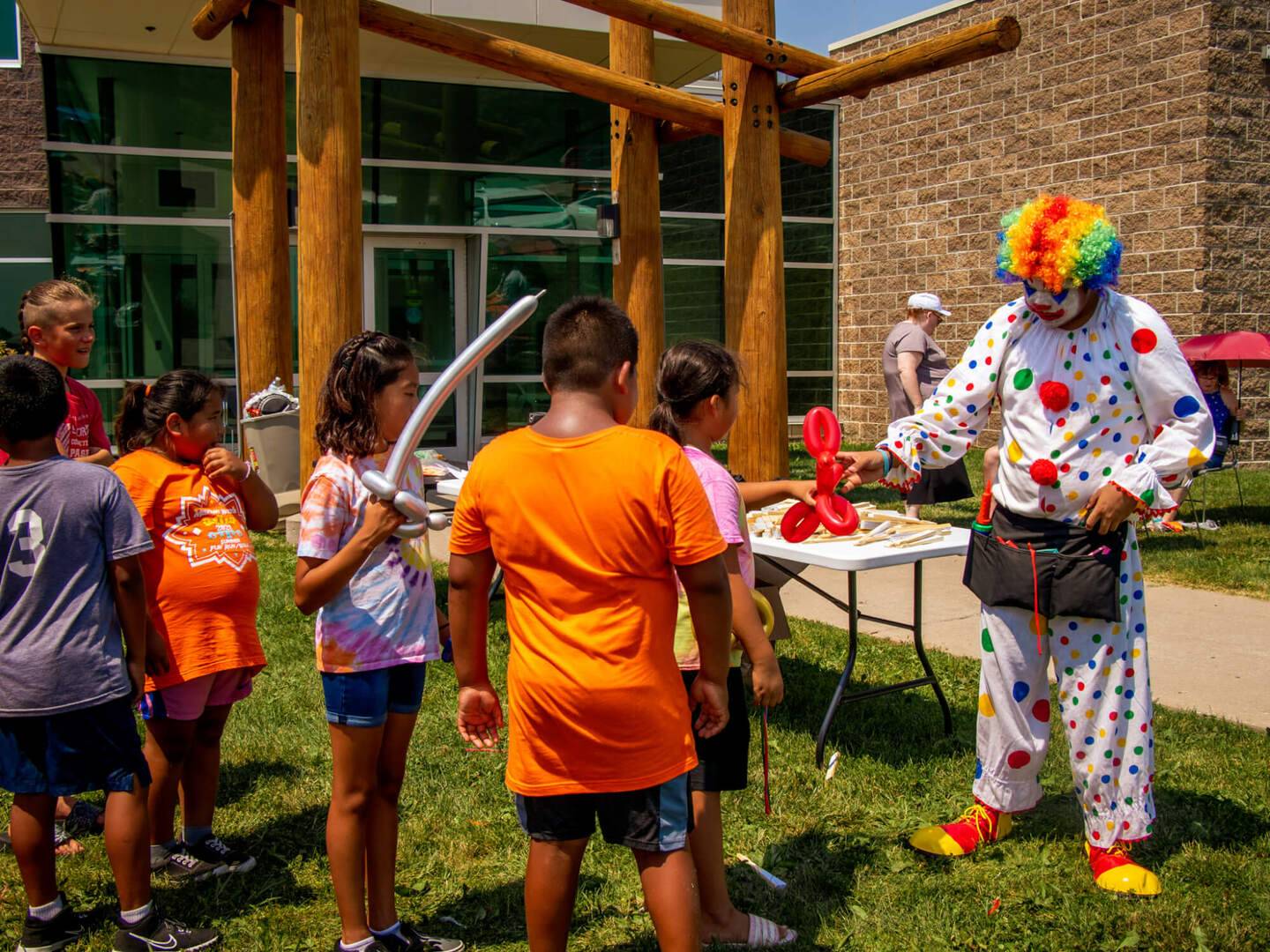 Children receiving balloon animals from a clown at the annual health clinic barbecue