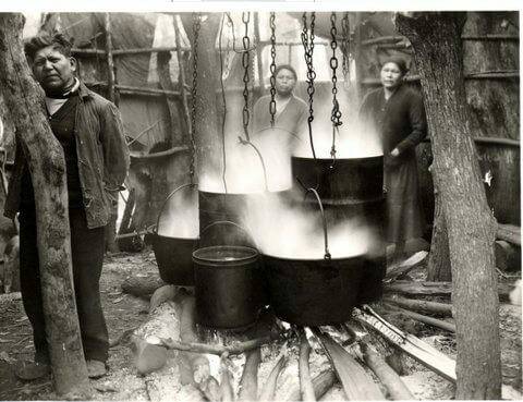 Vintage photo of a Man and two women standing around pots steaming inside a hut